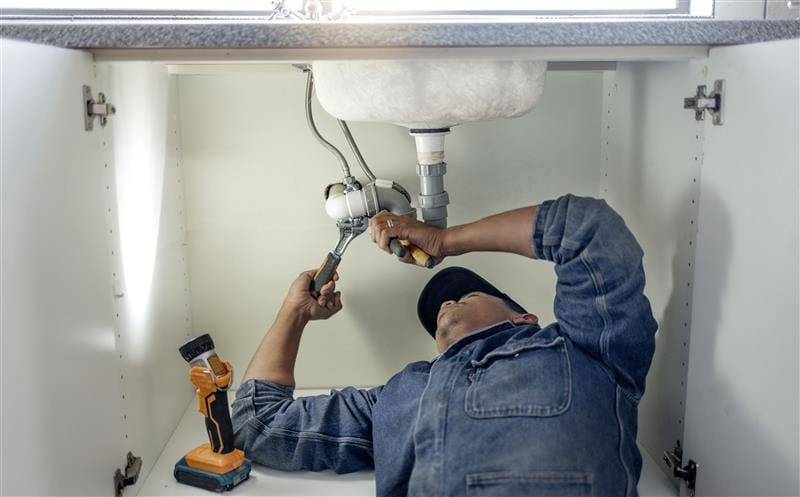 Plumber repairing pipes beneath a bathroom sink in Palm Beach Gardens