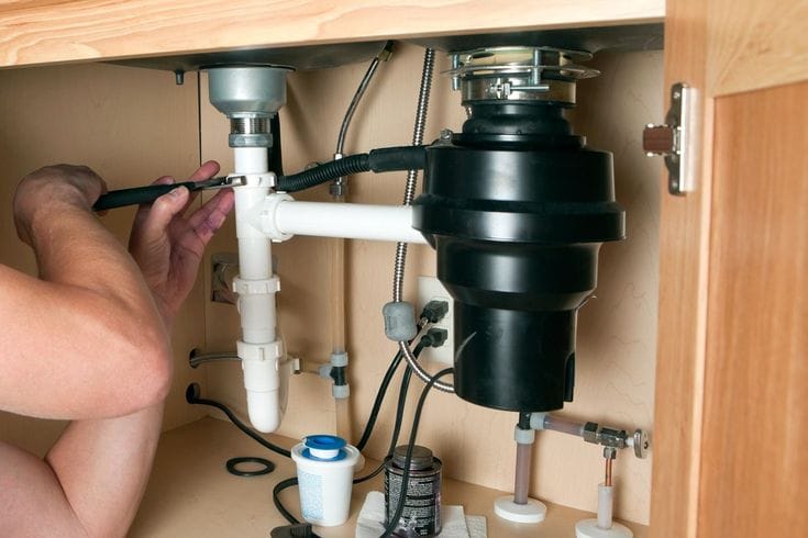 Plumber installing a garbage disposal beneath a kitchen sink in Palm Beach Gardens