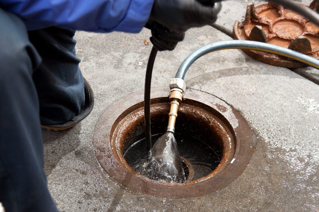 Plumber hydro jetting a sewer line through a manhole in Palm Beach Gardens