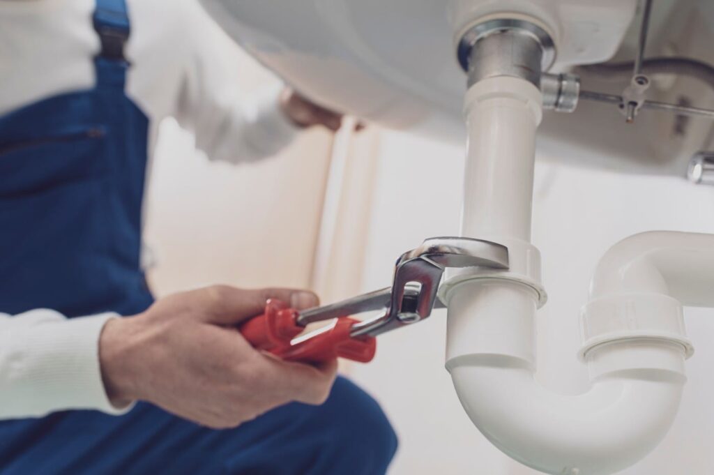 Plumber repairing a white drain pipe beneath a sink in Palm Beach Gardens