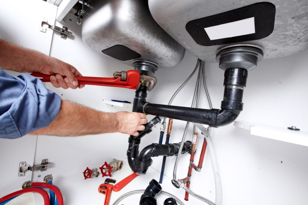 Plumber repairing drain pipes beneath a kitchen sink in Palm Beach Gardens