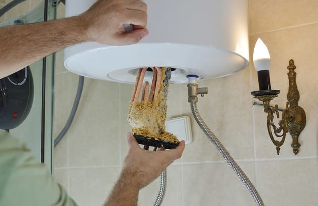 Technician removing mineral buildup from a water heater in Palm Beach Gardens